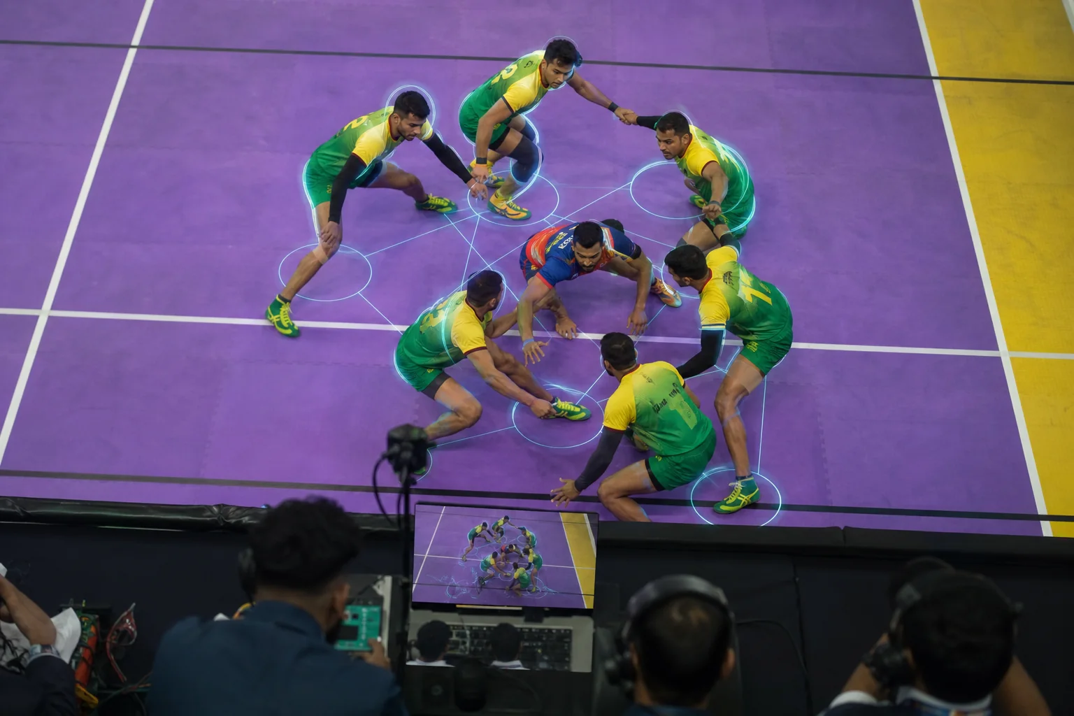 An overhead kabaddi match view showing a raider surrounded by overlapping defenders on a marked kabaddi court, with tracking outlines