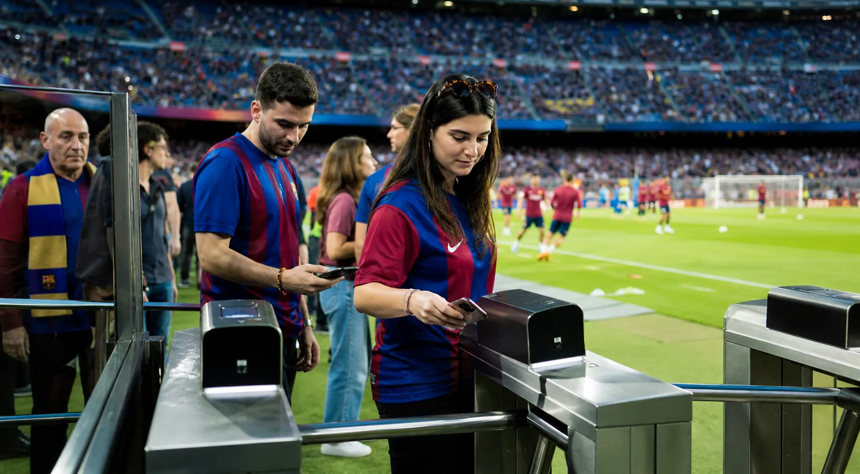 Fans in club jerseys scanning mobile tickets at stadium turnstiles, with a recognisable football or cricket pitch visible beyond the gate