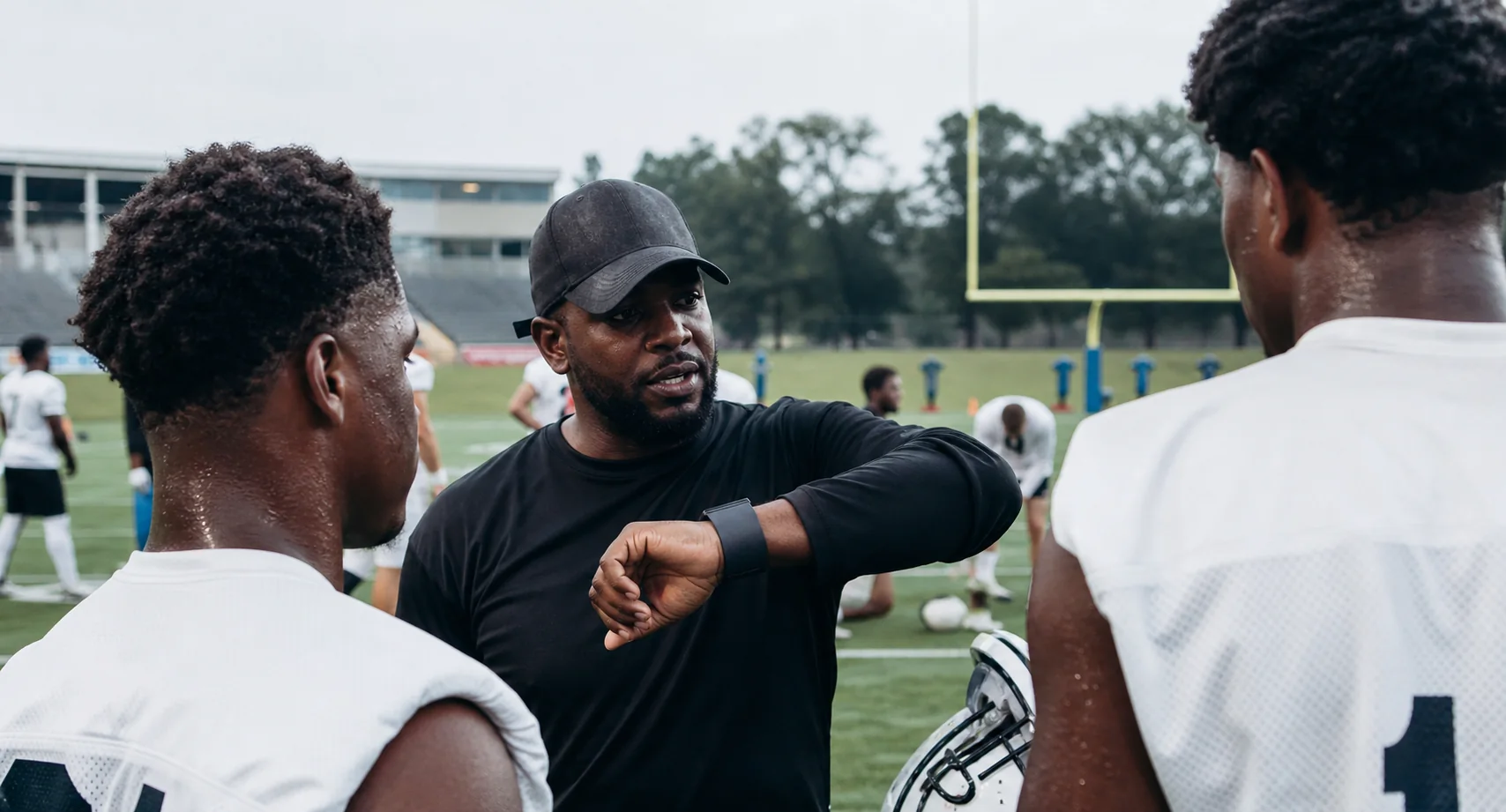 A coach giving a concise wearable-based cue to players during a visible football or rugby practice drill